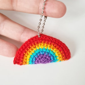 Könnte beinhalten: Ein gehäkelter Regenbogen-Schlüsselanhänger mit einer silbernen Kette. Der Regenbogen ist aus rotem, orangefarbenem, gelbem, grünem, blauem und violettem Garn gefertigt.