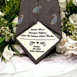 Könnte beinhalten: Eine schwarze Krawatte mit Paisley-Muster und einem weißen Etikett. Das Etikett trägt den Text "Heute Braut Morgen Ehefrau Aber für immer deine Tochter" und "Danke für alles Deine Michaela".