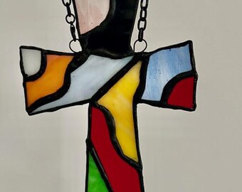 Peut inclure: Une croix en vitrail avec un cadre et une chaîne en métal noir. Le verre est multicolore avec des nuances de rouge, jaune, bleu, vert, orange et blanc.