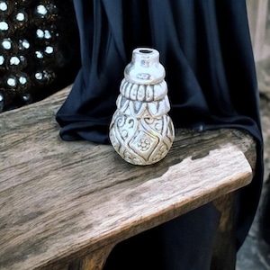 Peut inclure: Un bouchon de bouteille décoratif en argent avec un design complexe. Le bouchon est en forme de poire et présente un motif détaillé de volutes et de fleurs.