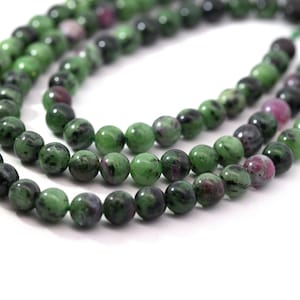 Könnte beinhalten: Nahaufnahme einer Halskette oder eines Armbands aus runden Perlen. Die Perlen sind eine Mischung aus Grün, Dunkelgrau und Rosa. Die Perlen sind aufgefädelt und bilden eine Halskette oder ein Armband. Die Perlen haben eine polierte, glatte Oberfläche.