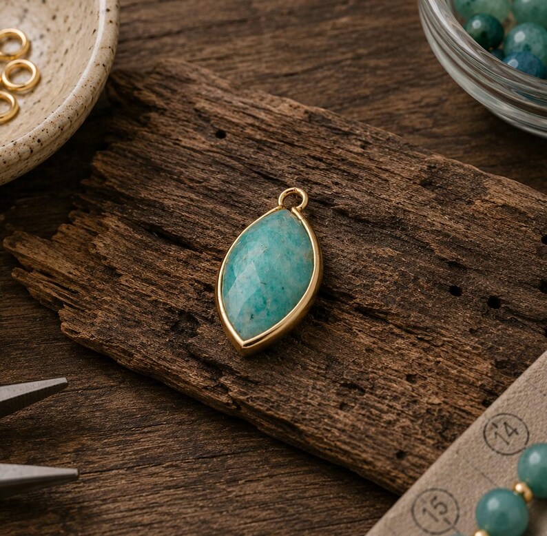 May include: A marquise-shaped pendant featuring a faceted teal amazonite stone set in a smooth gold-toned metal bezel. The pendant includes a small circular jump ring at the top for attachment, showcasing a polished finish and natural stone texture.