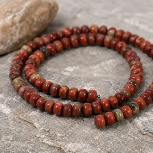 Peut inclure: Un collier de perles rondes en forme de disque dans des tons rouge profond, rouille et brun terreux. Les perles sont disposées en spirale circulaire, présentant une texture lisse et polie avec des variations de couleur et des motifs naturels.