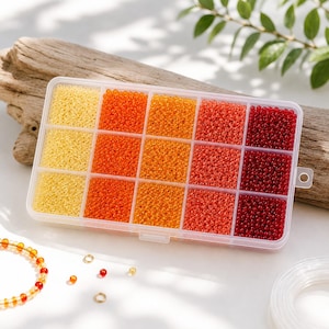 Pode incluir: Um recipiente de armazenamento retangular de plástico transparente com quinze compartimentos individuais preenchidos com pequenas contas redondas em um gradiente de cores que vai do amarelo pálido ao laranja brilhante, coral e vermelho escuro.