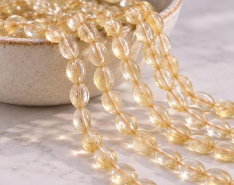 May include: A collection of translucent, oval-shaped yellow citrine beads strung together in multiple strands. The beads exhibit a smooth, polished finish with natural internal inclusions, reflecting light to create a bright, golden appearance.