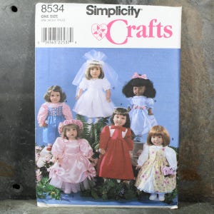 May include: A Simplicity Crafts sewing pattern with doll designs. The cover shows six dolls in different outfits, including a wedding dress, a pink dress, and a red dress. The cover has the text "Simplicity Crafts" and the pattern number 8534.
