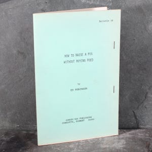 Op de afbeelding: Een lichtblauw boekje met de titel "HOW TO RAISE A PIG WITHOUT BUYING FEED" door ED ROBINSON. Het boekje wordt uitgegeven door GARDEN WAY PUBLISHING in CHARLOTTE, VERMONT 05445. Het boekje is gemarkeerd als Bulletin 18.