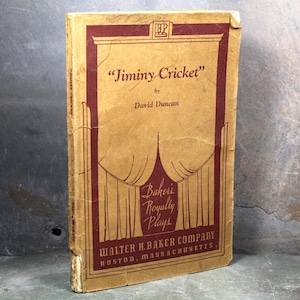 May include: A vintage book titled "Jiminy Cricket" by David Duncan. The cover is tan with maroon lettering and decorative elements. The book is part of Baker's Royalty Plays, published by Walter H. Baker Company in Boston, Massachusetts.