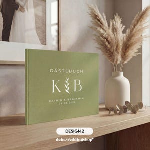 May include: A sage green guest book with the text "G&auml;stebuch" and the initials "K & B" in white. The names "Katrin & Benjamin" and the date "06.06.2026" are also printed on the cover. The book is displayed on a wooden surface.