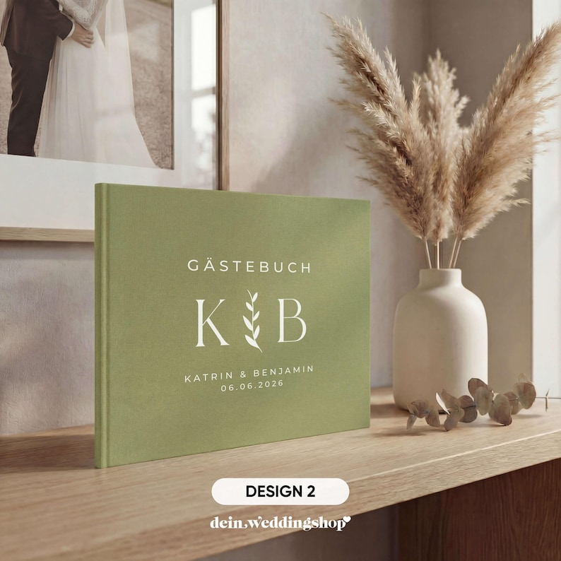 May include: A sage green guest book with the text "G&auml;stebuch" and the initials "K & B" in white. The names "Katrin & Benjamin" and the date "06.06.2026" are also printed on the cover. The book is displayed on a wooden surface.