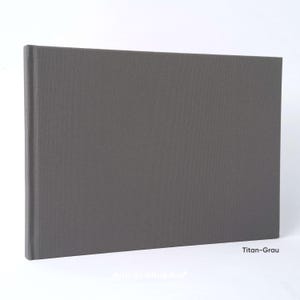 May include: A rectangular, gray photo album with a textured cover. The album is closed and has a spine on the left side. The text "Titan-Grau" is visible in the lower right corner.