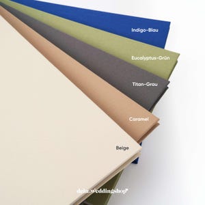 May include: A stack of paper in various colors, including beige, caramel, titan gray, eucalyptus green, and indigo blue. Each sheet is labeled with its color name. The bottom sheet has the text "dein.weddingshop".