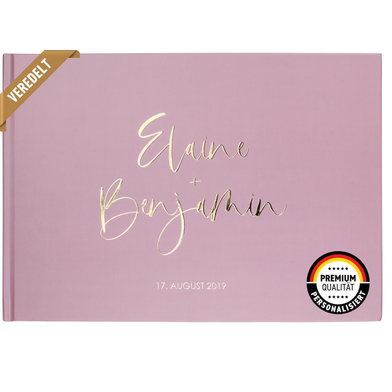 May include: A dusty rose colored guest book with gold foil lettering that reads "Elaine + Benjamin" and "17. AUGUST 2019". The book has a gold foil sticker that reads "VEREDELT" on the top left corner and a gold foil sticker that reads "PREMIUM QUALITAT PERSONALISIERT" on the bottom right corner.
