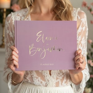 May include: A dusty rose colored guest book with gold foil lettering that reads "Elaine + Benjamin 17. AUGUST 2019".