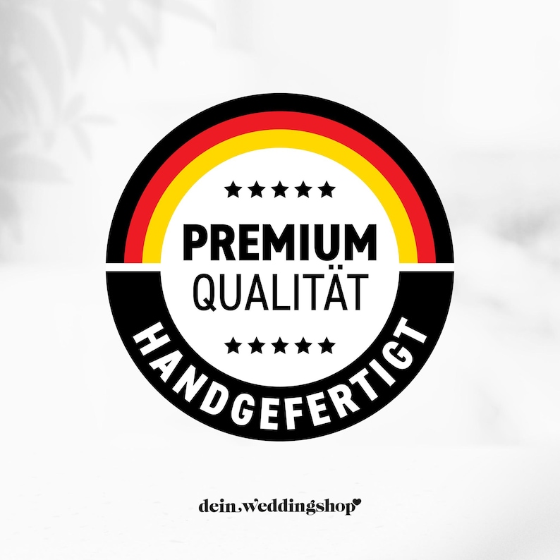 May include: A circular emblem with the German flag colors, black, red, and yellow. The words "PREMIUM QUALIT&Auml;T" and "HANDGEFERTIGT" are in white text. The emblem also includes the text "dein.weddingshop".