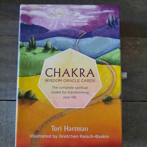 May include: A Chakra Wisdom Oracle Cards box set. The box features a colorful landscape illustration with a winding road, hills, and a sunset. The text on the box reads "CHAKRA WISDOM ORACLE CARDS" and "The complete spiritual toolkit for transforming your life."