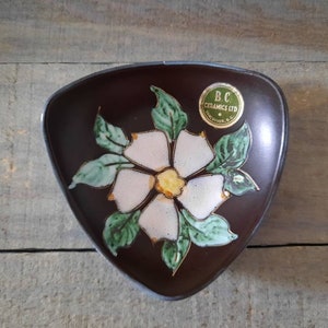 May include: A brown, triangular ceramic dish with a white flower design and green leaves. The dish has a blue rim and a gold sticker that reads "B.C. Ceramics Ltd. Vancouver, B.C."