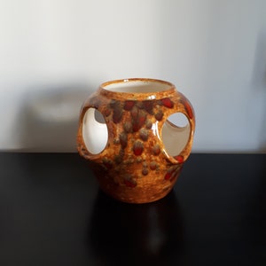 May include: A ceramic vase with a unique design. The vase is primarily brown with red and dark brown accents. It features three large, circular openings and a white interior. The vase sits on a black surface.