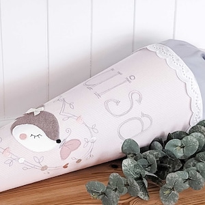 May include: Pink and gray school cone with a cute embroidered deer and butterfly design. The cone has a white lace trim and the word "Schule" embroidered on it.