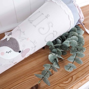 May include: A light pink and gray fabric cone with a white lace trim and a cute embroidered fox design. The cone has the word "Liso" embroidered on it.