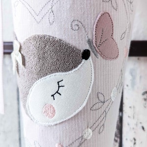 May include: Pink and gray embroidered tights with a cute little mouse design. The mouse has a pink nose and a closed eye. The tights are decorated with a butterfly and hearts.