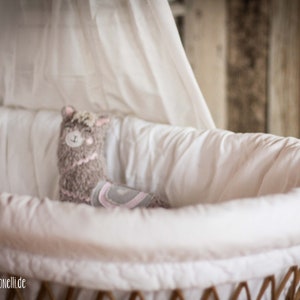 May include: A white wicker bassinet with a white canopy and a plush gray llama toy inside.