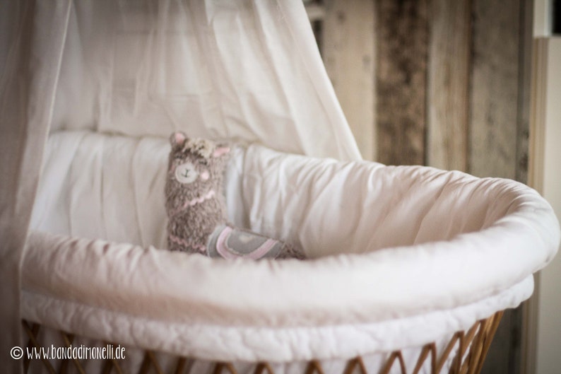 May include: A white wicker bassinet with a white canopy and a plush gray llama toy inside.