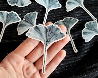 May include: A set of black and white ginkgo leaf stickers. The stickers are on a black fabric background.