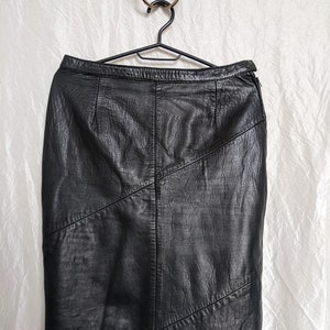 May include: A black leather skirt with a straight cut and a geometric design. The skirt has a zip fastening and a waistband.