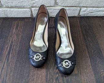 May include: A pair of black leather heeled pumps with a silver MK logo on the front.