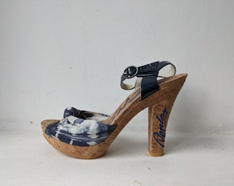 Puede incluir: Sandalias de cuña de corcho con estampado azul y blanco, con una correa de tobillo negra y la palabra "Replay" escrita en el talón.