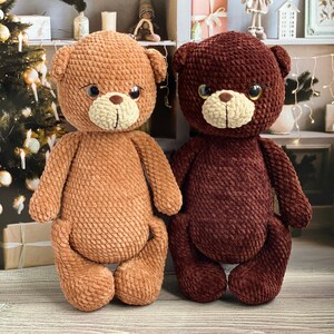 May include: Two handmade crochet teddy bears. One is light brown, the other is dark brown. Both have cream-colored snouts and large, expressive eyes. The bears are sitting side-by-side, showcasing their soft, textured bodies.