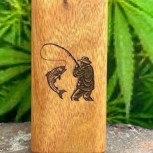 May include: A rectangular wooden box with a light brown grain finish featuring a laser-engraved illustration on the front. The design depicts a person wearing a hat and jacket while fishing with a rod, successfully catching a large jumping fish.