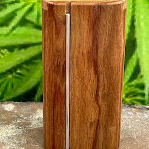May include: A rectangular wooden case with a smooth, polished finish and visible natural grain patterns. A thin, vertical silver-colored metal rod is embedded into a narrow groove running down the center of the front face of the wooden object.