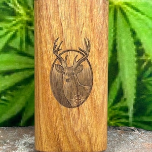 May include: A rectangular wooden box with a deer head etched into the front. The deer is inside a circular frame. The wood has a natural grain and a warm, brown color. The box is standing upright.