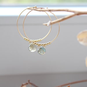 May include: Gold hoop earrings with a small, light green gemstone dangling from each hoop.