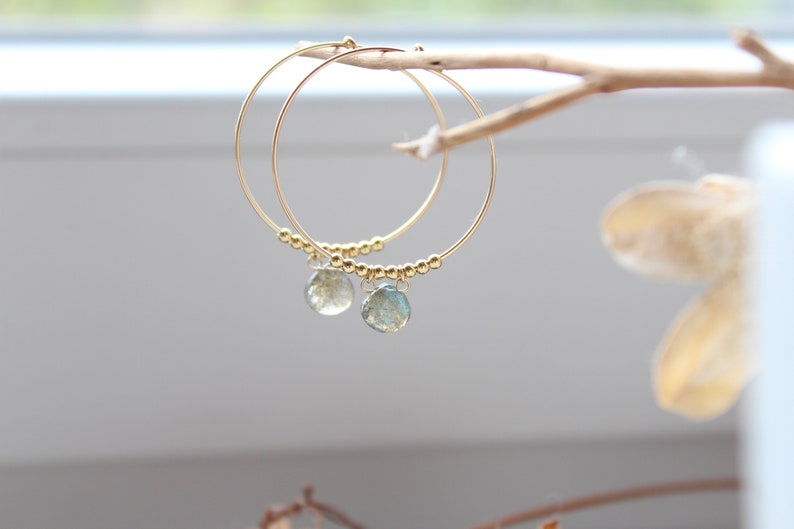 May include: Gold hoop earrings with a small, light green gemstone dangling from each hoop.