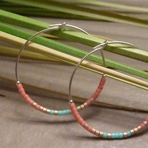 May include: A pair of silver hoop earrings with a beaded design. The beads are pink, turquoise, and gold.