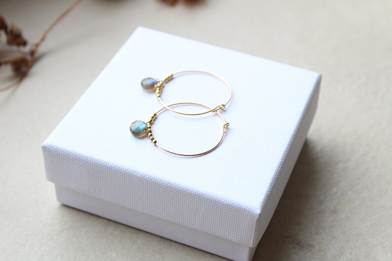May include: A pair of gold hoop earrings with a small, iridescent blue gemstone dangling from each hoop.