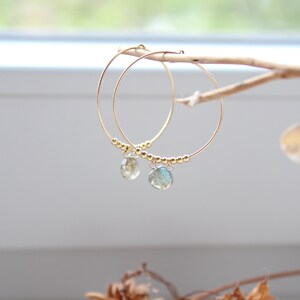 May include: Gold hoop earrings with a teardrop-shaped gemstone dangling from each hoop.