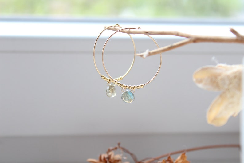 May include: Gold hoop earrings with a teardrop-shaped gemstone dangling from each hoop.