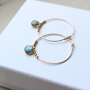 May include: Gold hoop earrings with a small blue-green gemstone dangling from each hoop.