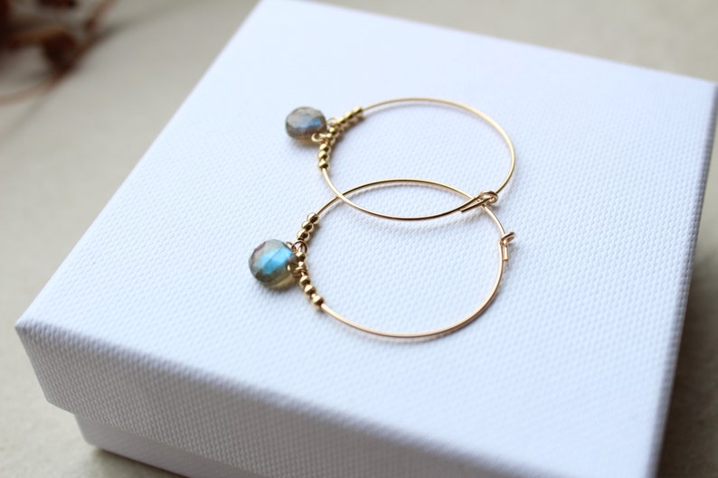 May include: Gold hoop earrings with a small blue-green gemstone dangling from each hoop.