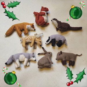 May include: A collection of handmade knitted woodland animal figurines, including a fox, squirrel, deer, badger, wolf, rabbit, and boar. Each animal is crafted with detailed features and various colors. Festive holiday decorations are in the background.