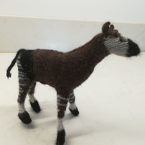 May include: A brown and white knitted stuffed animal resembling an okapi, a type of mammal native to the Democratic Republic of Congo. The animal has a long neck, a striped body, and a black nose.