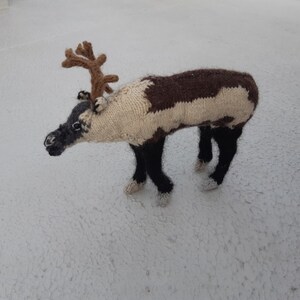 May include: A knitted reindeer toy with brown and white fur, black legs, and brown antlers.