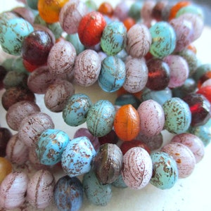 Könnte beinhalten: Nahaufnahme einer Reihe bunter Glasperlen. Die Perlen sind rund und haben eine gesprenkelte, strukturierte Oberfläche. Die Farben umfassen Blau, Grün, Rosa, Orange und Braun.