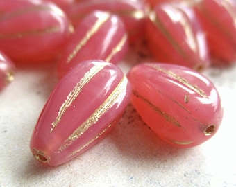 May include: Close-up of several pink, oval-shaped beads with gold stripes. The beads have a glossy finish and a hole drilled through each end. These beads are suitable for jewelry making.