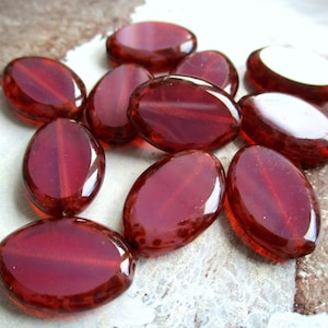 Könnte beinhalten: Eine Gruppe ovaler Glasperlen in einem tiefen Rot mit einem subtilen Schimmer. Die Perlen haben eine glatte, polierte Oberfläche und sind perfekt für die Schmuckherstellung oder das Basteln.