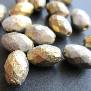 May include: A group of oval-shaped glass beads with a textured, metallic finish. Some beads are gold, while others are silver.